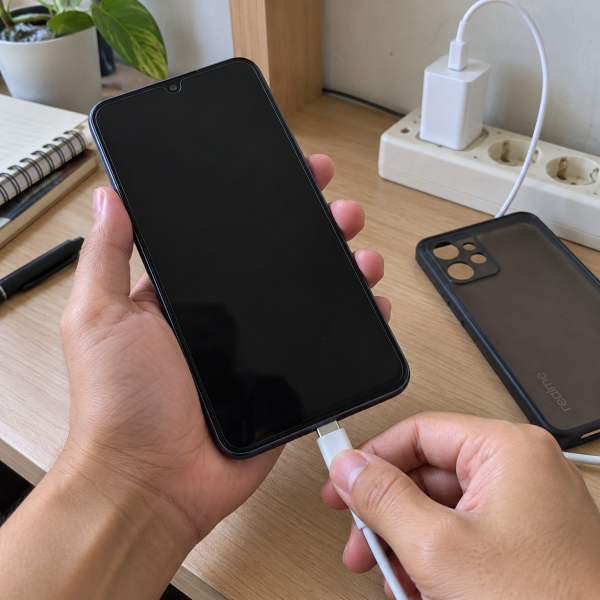 HP realme dengan layar hitam sedang disambungkan ke charger tetapi belum menunjukkan respons.
